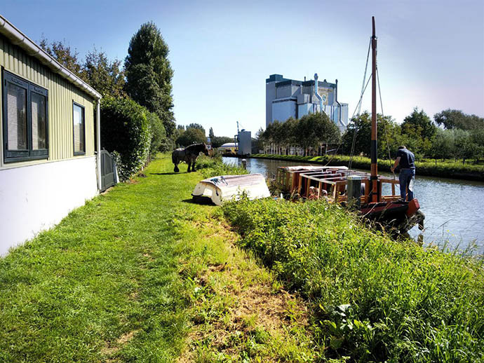 Foto van de oever van de Hollandse IJssel met een gerenoveerde trekschuit, met op de oever een werkpaard.